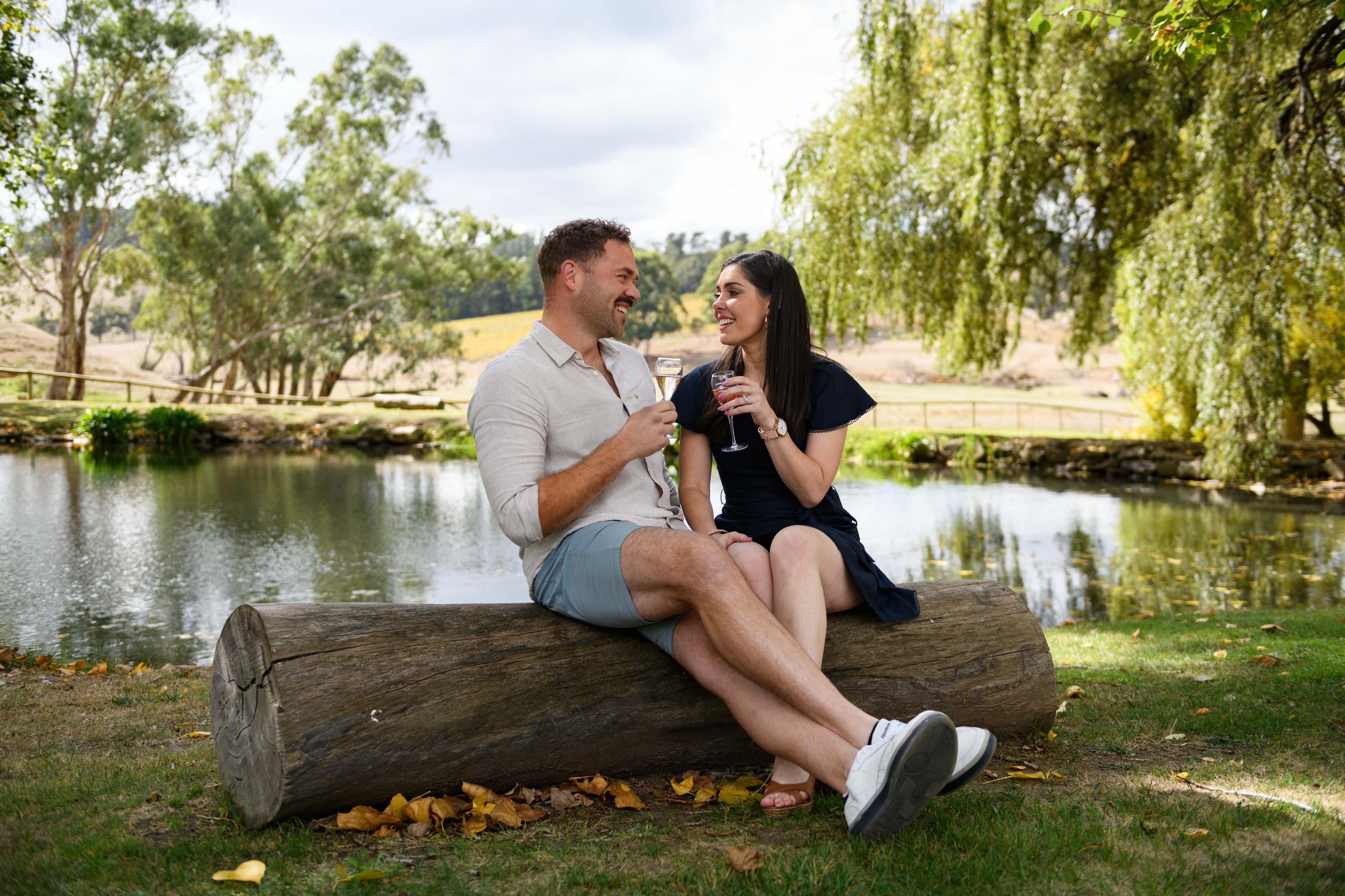 A man and a woman sitting on a log enjoying wine 